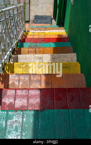 Vibrant multi colored steps on a narrow urban staircase in Istanbul, showing bright red, yellow, orange, and green bricks under warm sun shadows Stock Photo
