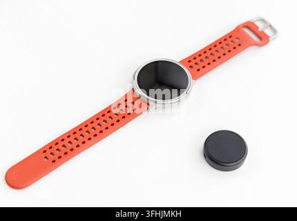 A modern smartwatch with an orange band rests on a white surface Stock Photo
