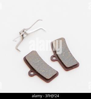 Two bicycle disc brake pads and a spring clip sit on white Stock Photo