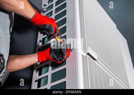 Close view of gloved hands using a screwdriver on the casing of an outdoor HVAC unit. Stock Photo
