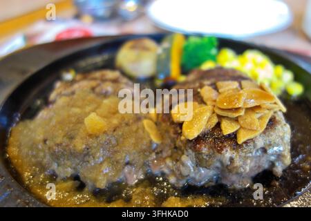 Delicious double hamburg steak served on a hot sizzling iron plate, garnished with crispy garlic chips, grated onion sauce, and fresh vegetables like Stock Photo