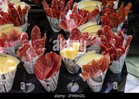 Assorted charcuterie cones filled with sliced cured meats, salami and cheese displayed on a busy market stand in Barcelona, Spain. Perfect for tapas, Stock Photo