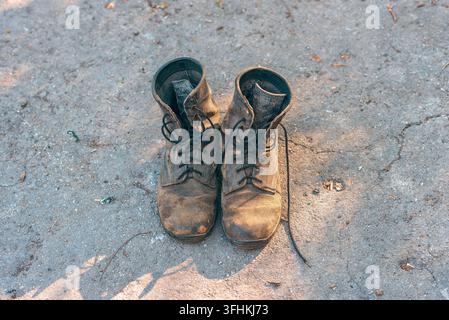 Top view of old worn leather boots standing on ground outdoors. Old laces untied and worn texture. Stock Photo