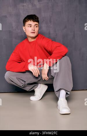 A young, handsome man confidently poses in a red sweater and stylish gray pants. Stock Photo