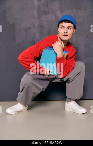 A fashionable young man crouches while holding colorful notebooks. Stock Photo