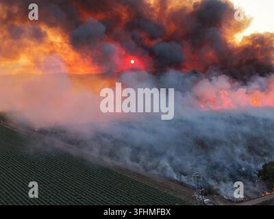 Aerial view of a sugarcane field fire burning at sunset with thick smoke and flames rising over the agricultural landscape in Home Hill, Queensland, A Stock Photo