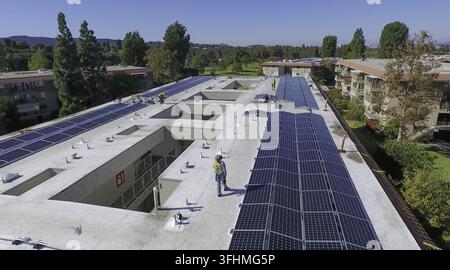 Aerial view of workers installing solar panels on the flat roof of an apartment building in Tustin, CA, USA. Stock Photo