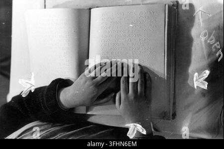 A person reading a book printed in Braille, 1941, with two hands resting on the open book, the hands positioned as if reading by touch. Stock Photo