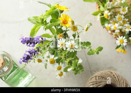 Different aromatic herbs with beautiful flowers in vase, wicker basket, bottle of essential oil and rope on gray table, flat lay Stock Photo