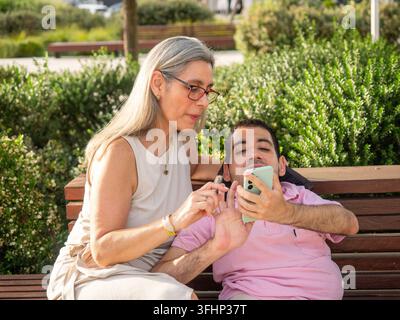 Woman and man with disability using a mobile phone together on a park bench Stock Photo