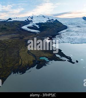 Aerial view of Fjallsarlon glacier lagoon featuring the massive glacier tongue, floating icebergs, and glacial meltwater flowing through the rugged vo Stock Photo