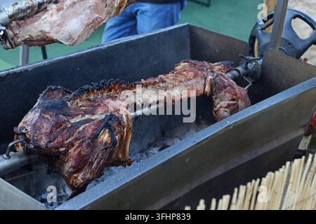 Whole lamb roasting on a metal spit over charcoal at a traditional Portuguese food fair, with browned meat and charred edges visible along the carcass Stock Photo