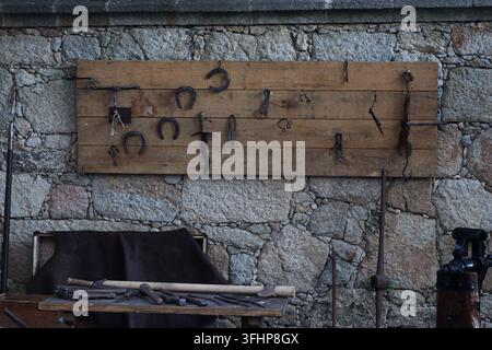 Traditional blacksmith tools displayed on a wooden board against a rough stone wall, with hammers, tongs, chisels and other ironworking implements arr Stock Photo