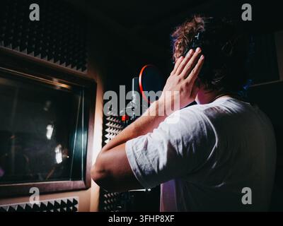Young handsome singer man puts on headphones in the studio. Recording new melody or album. Male vocal artist with curly hair pre Stock Photo