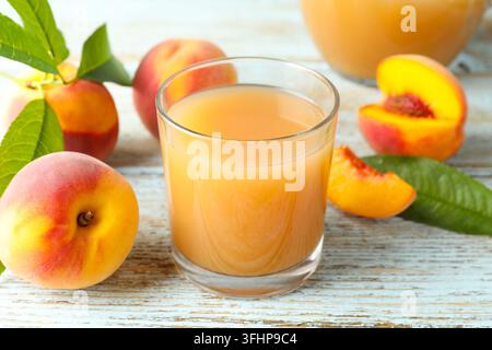 Tasty juice in glass and jug with peaches on light wooden table, closeup Stock Photo
