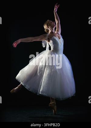 Graceful ballerina in white tutu dress dancing elements of classical or modern ballet in the dark with neon light and smoke on t Stock Photo