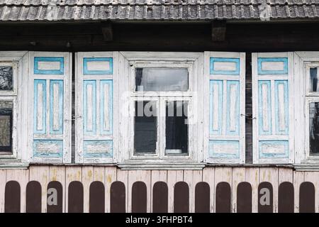 Old wooden house windows with blue shutters and weathered facade. Architecture background for rural heritage folk design and traditional homes. Stock Photo