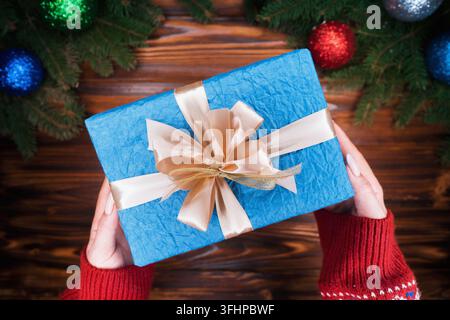 Top view. Woman's hands with gift wrapped in blue paper with golden ribbon. Wooden vintage table. Beautiful holidays background Stock Photo