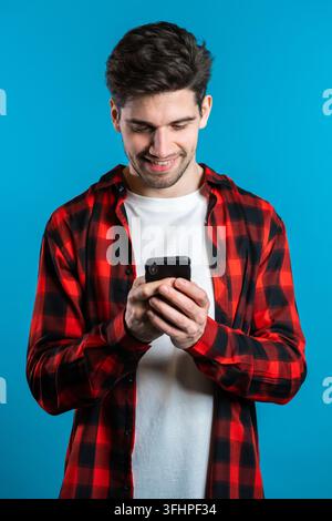 Man sms texting using app on smartphone. Handsome young guy surfing internet with mobile phone. Blue studio background Stock Photo