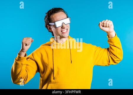 Hipster man in glowing glasses moving to the music rhythm on blue studio background. Dancing positive comic guy Stock Photo