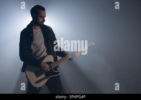 Rock guitarist man in leather jacket in smoky studio or stage masterfully playing electric guitar. View of musician in the spotl Stock Photo