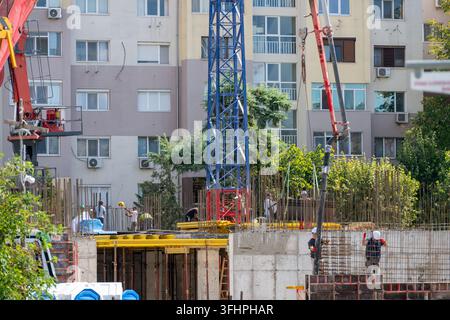 Construction workers poured concrete into reinforced building structures using a large pump boom and tower crane in an urban development zone. Stock Photo