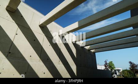 Concrete beams creating geometric shadows on a modern brutalist wall under a clear blue sky Stock Photo