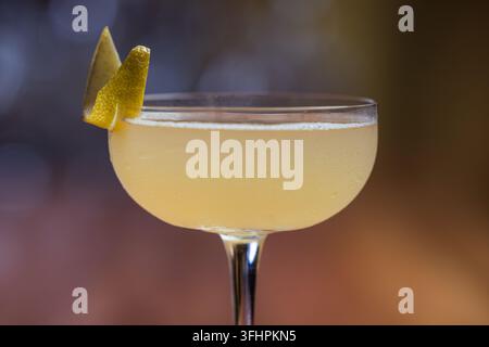 Elegant cocktail, the Bees Knees in coupe glass. Lemon twist adorns the rim. Warm wood table. Perfect for bar, lounge Stock Photo