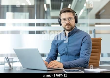 Remote work and customer support, professional man with headset working on laptop in modern office for business communication and virtual meeting. Digital connectivity and corporate productivity. Stock Photo