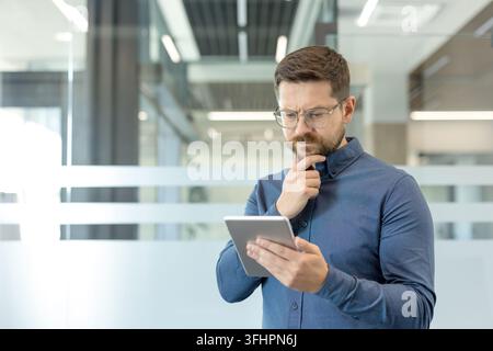 Business decision making and digital strategy, thoughtful man using a tablet in a modern office environment to analyze data and corporate growth. Stock Photo