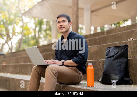 Asian businessman with reusable eco friendly ecological cup using laptop and sitting outside the office building. Eco friendly, Stock Photo