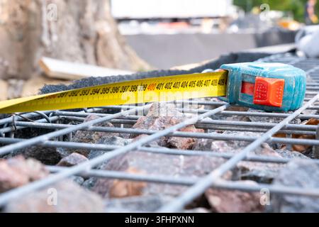A close-up shot of an open yellow tape measure placed on top of a steel wire mesh gabion wall filled with granite stones at an outdoor construction si Stock Photo