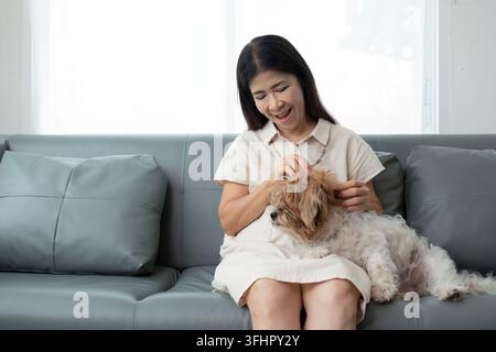 Elderly asian woman happy and a dog in the morning at home indoor, single senior retired female sitting on sofa in living room Stock Photo