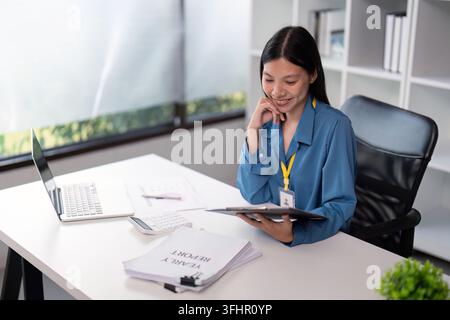 Businesswoman reviewing documents at desk with laptop in modern office. Concept of professional analysis and productivity Stock Photo