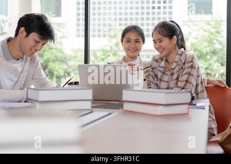 A group of cheerful students collaborating on a project with laptops and books in a bright, modern classroom setting. Stock Photo