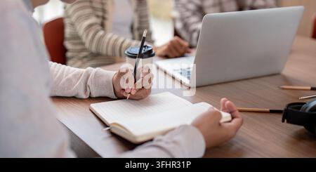 Students collaborating on a project, using laptops and notebooks, in a modern classroom environment. Stock Photo