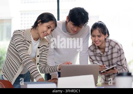 Three students working together on a laptop, engaged in a collaborative project in a bright, modern classroom environment. Stock Photo