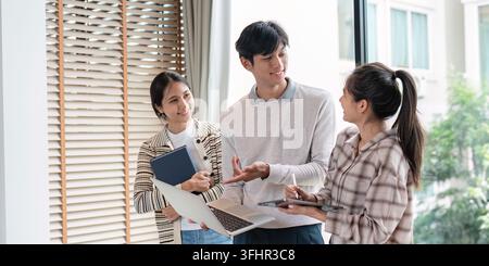 Three students engaged in a lively discussion, sharing ideas and working together in a bright, modern study environment. Stock Photo