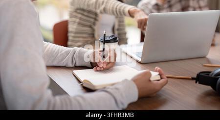 Students engaged in collaborative study session, using laptops and notebooks in a modern classroom environment. Stock Photo