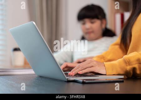 Focused hands typing on laptop with daughter watching Stock Photo