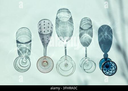 Empty glasses of different forms for white, red and rose wine stand in row on blue background in sunlight with shadows. Top view Stock Photo