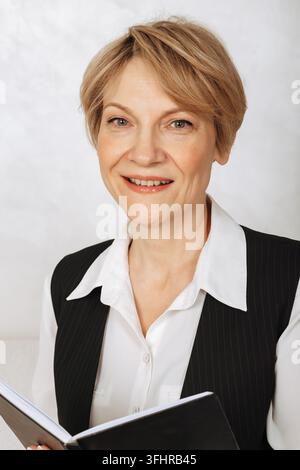 Portrait of business woman. Confident, successful mature woman holding black diary on light gray background. Looking at camera Stock Photo
