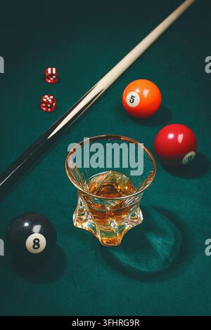 A glass with a drink sits on a green felt table. Nearby are billiard balls marked with numbers 5, 7, and 8. Two dice are placed next to the balls Stock Photo