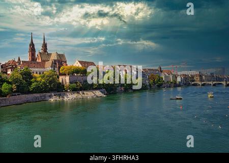 Dramatic river view with church buildings and impressive cloud formations, sunbeams breaking through, Rhine, Middle Rhine Bridge, Basel Cathedral, Bas Stock Photo
