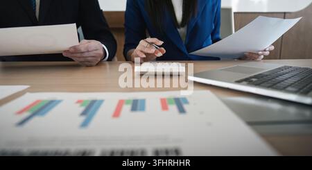 Close-up of a diverse business team reviewing financial documents and calculating data in a modern office environment. Stock Photo