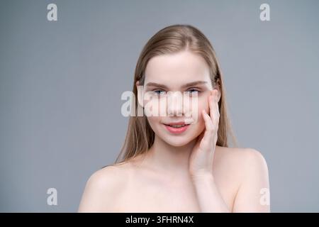 A woman with long blonde hair is smiling and touching her face Stock Photo