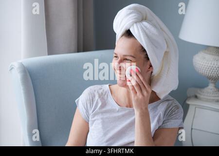Smiling woman with towel on her head and in bathrobe holding cotton pad pad Stock Photo