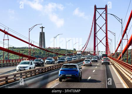 Distinctive red suspension bridge Ponte 25 de Abril, which straddles the Tagus River. In the background on the right is also the Cristo Rei monument i Stock Photo
