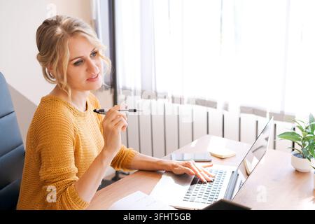 Attractive european business woman is on phone and taking notes at same time writing down important information. Modern electronic gadgets and communi Stock Photo