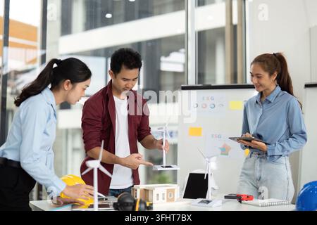 A diverse group of engineers collaborates on a sustainable energy project, showcasing wind turbines and eco-friendly designs in a bright office space. Stock Photo